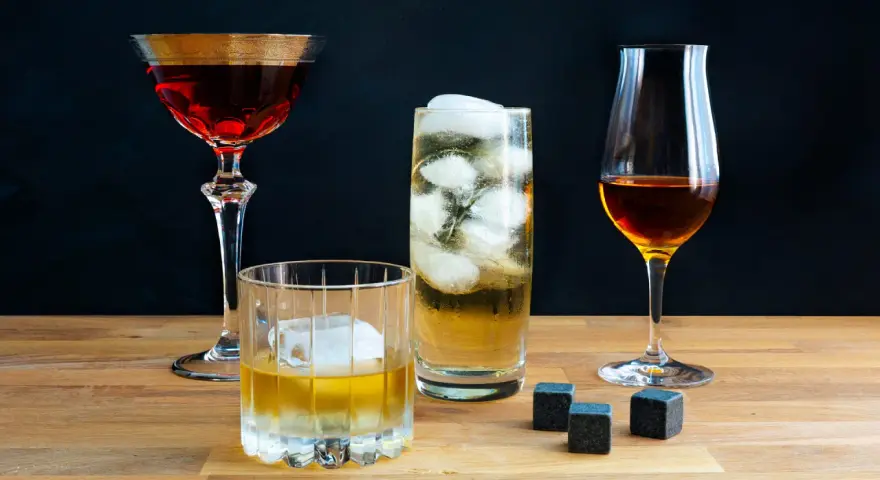 Vier Gläser mit verschiedenen Getränken, darunter ein Whisky-Cocktail, ein Highball und ein Nosing-Glas. So trinkt man Whisky: pur, mit Eis oder als Mixgetränk.