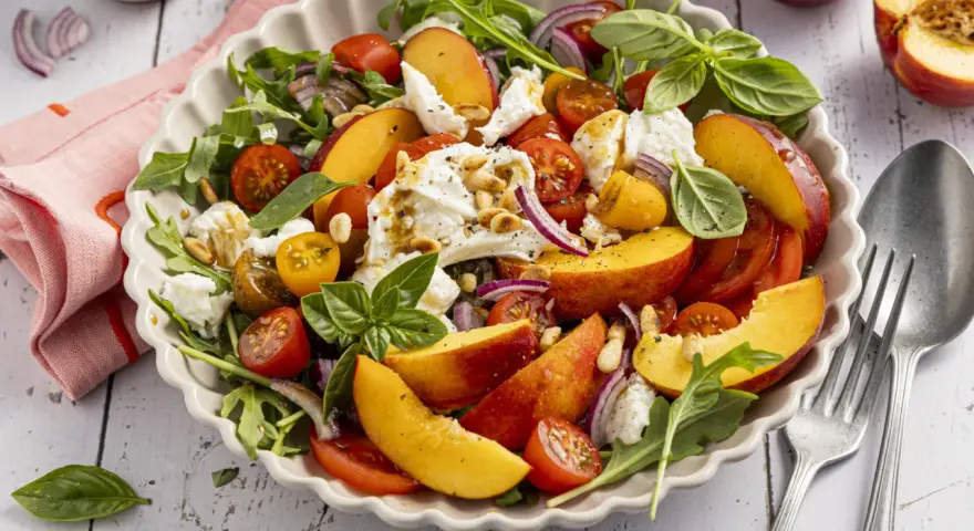 Erfrischender Salat mit saftigen Nektarinen, Tomaten, Mozzarella und Rucola, beträufelt mit Balsamico-Dressing.