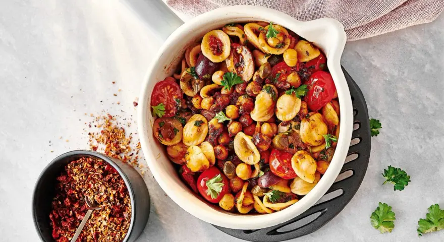 Ein bunter Nudelsalat mal anders: Orecchiette mit Kichererbsen, Kirschtomaten, Oliven und Kräutern in einer Auflaufform. Daneben eine Schale mit Gewürzmischung.
