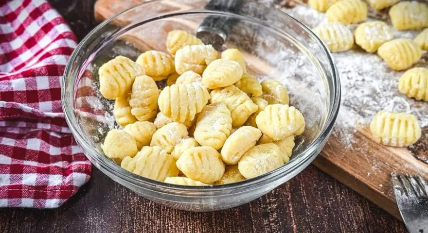 Frisch gemachte Gnocchi in einer Schüssel, bereit zum Kochen. Auf dem Holzbrett liegen weitere Gnocchi, die zeigen, wie einfach es ist, Gnocchi selber machen.