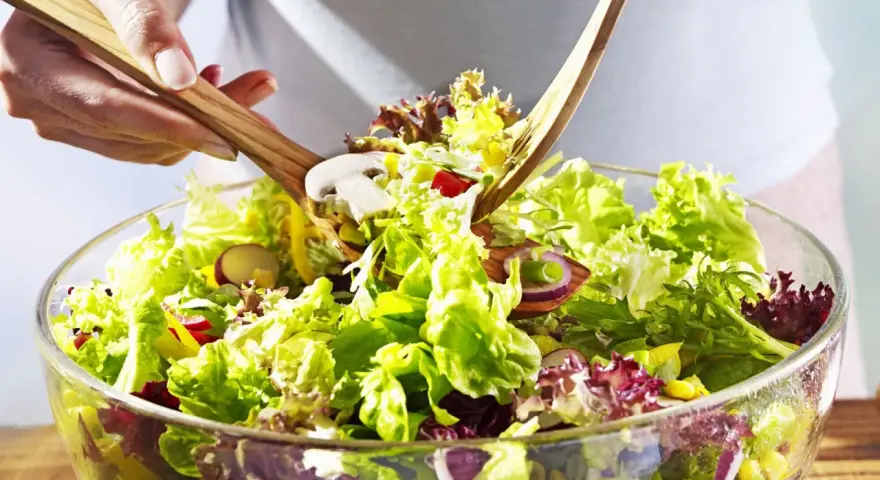 Frischer gemischter Salat mit knackigem Salat, Radieschen, Zwiebeln und Pilzen wird mit Holzsalatbesteck vermischt.