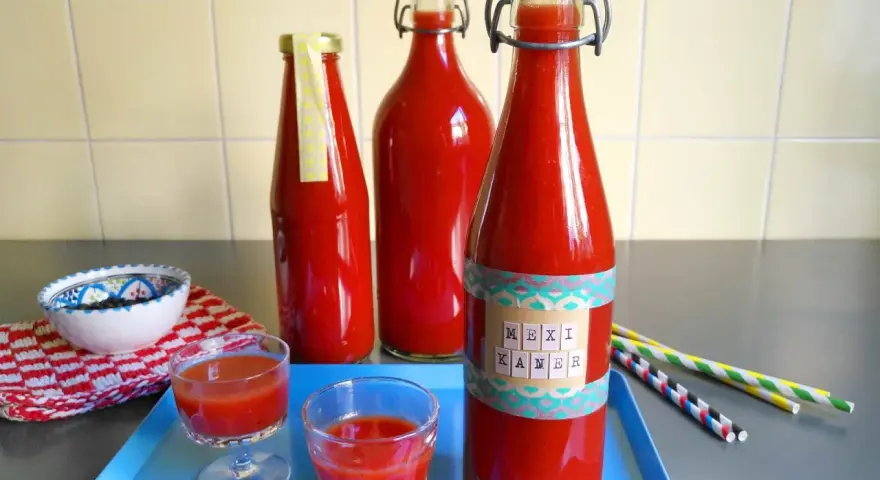 Rot gefüllte Flaschen mit dem Aufdruck "Mexikaner Rezept" und kleine Gläser mit dem Getränk.