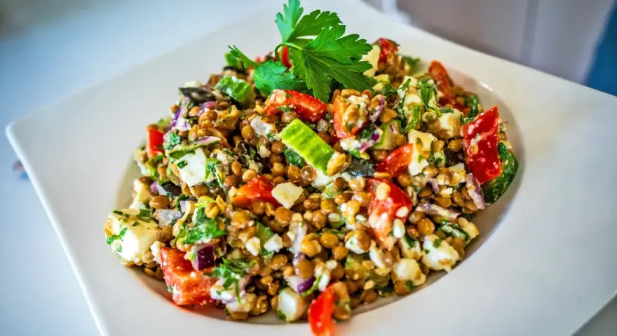 Frischer Linsensalat mit Feta, Paprika, Gurke und Kräutern, garniert mit Petersilie.