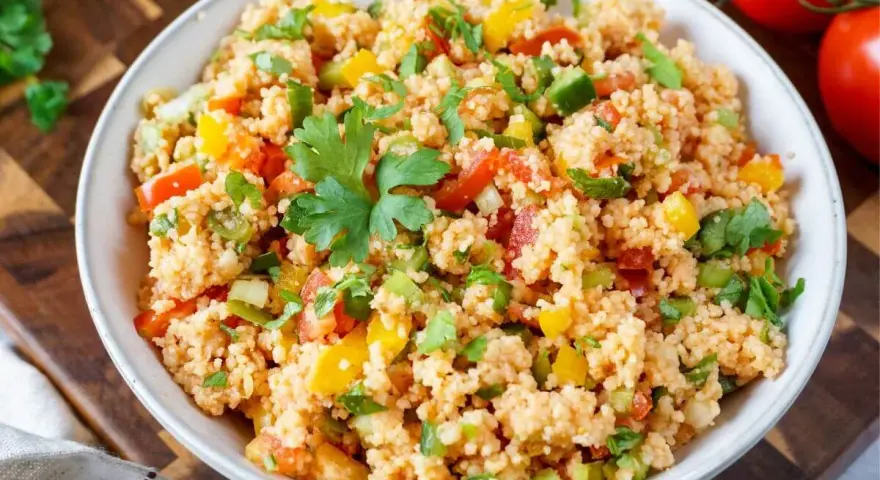 Bunter Couscous-Salat mit Tomaten, Paprika und Petersilie, garniert mit einem Petersilienblatt.
