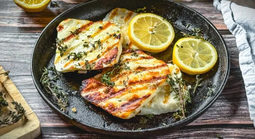 Perfekt gegrillter Halloumi mit Kräutern und Zitronenspalten auf einer Gusseisenplatte. Ein Genuss für alle Sinne!