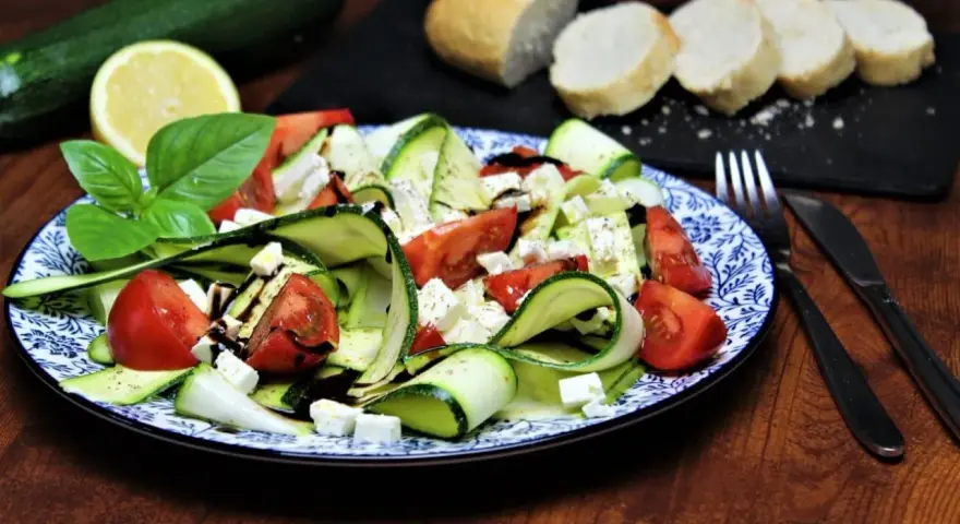 Ein erfrischender, sommerlicher Zucchini-Salat mit Tomaten und Feta, garniert mit Basilikum und Balsamico. Dazu Baguettescheiben.