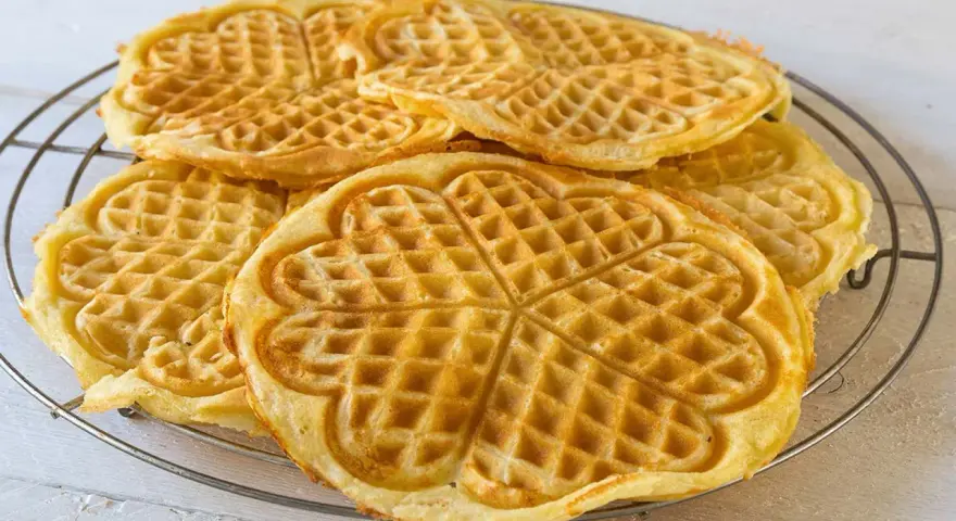 Goldbraune Herz-Waffeln, frisch gebacken aus waffelteig ohne butter, liegen auf einem Gitter.