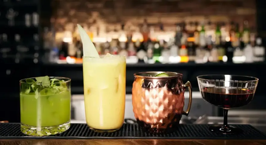 Vier kunstvoll zubereitete Cocktails, die die Definition eines perfekten Drinks verkörpern: ein grüner, ein gelber, ein Moscow Mule und ein dunkler Aperitif.