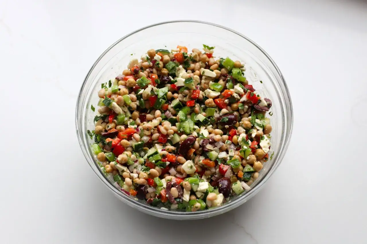 Frischer griechischer Bohnensalat in einer Glasschüssel mit Kichererbsen, weißen Bohnen, Gurken, Paprika, Feta und Oliven.
