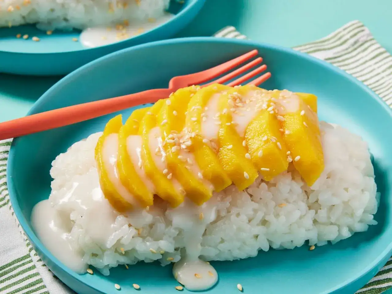 S&uuml;&szlig;er sticky rice mit Mango, &uuml;bergossen mit Kokosmilch und bestreut mit Sesam. Ein k&ouml;stlicher Nachtisch auf einem blauen Teller.