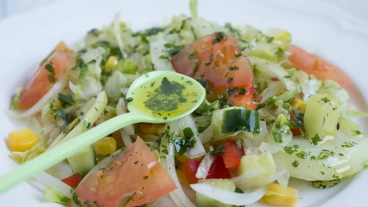 Frischer Salat mit Tomaten, Gurken und Mais. Eine L&ouml;ffelprobe zeigt die k&ouml;stlichen Dressing Ideen.