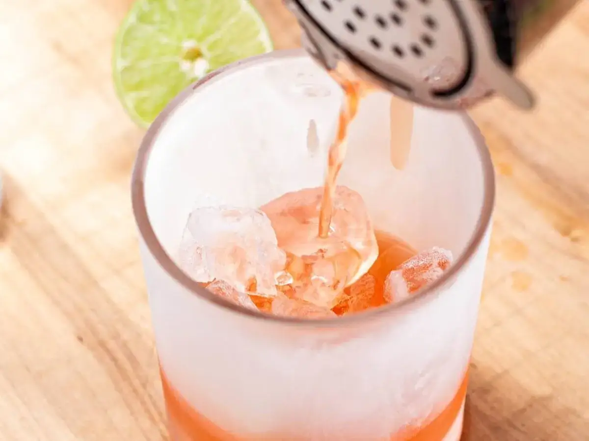 Ein rosafarbener Drink wird in ein Glas mit Eisw&uuml;rfeln gegossen. Dies ist die perfekte Cocktail-Definition f&uuml;r einen erfrischenden Genuss.