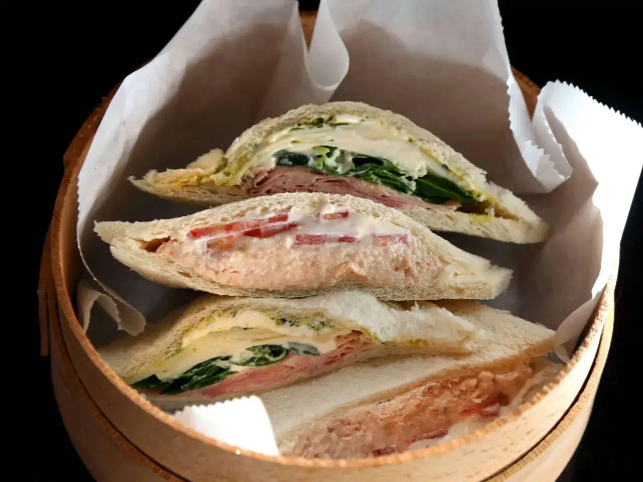 Drei Tramezzini-Sandwiches mit Schinken, Salat und Tomaten-Creme in einem Holzkörbchen. Inspiration für Tramezzini Rezepte.