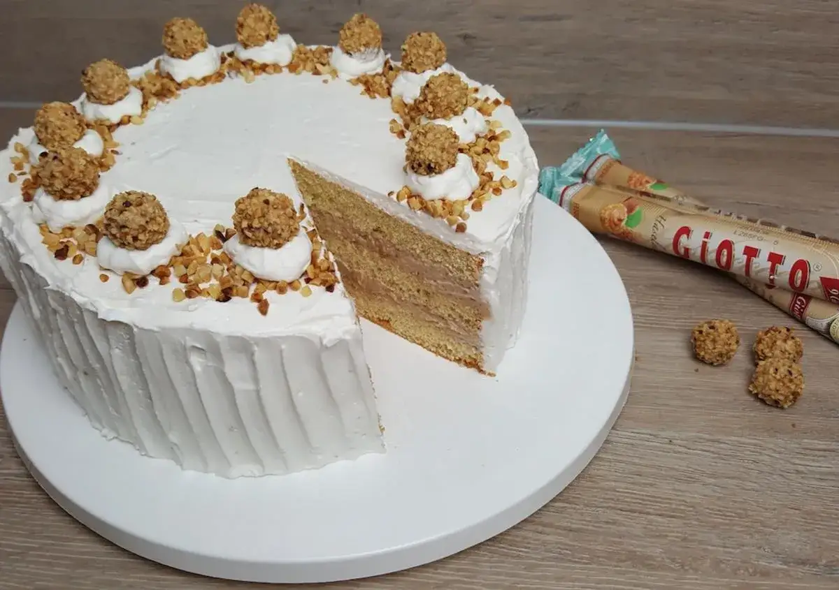 Eine k&ouml;stliche Giotto Torte mit wei&szlig;em Frosting, gehackten N&uuml;ssen und Giotto-Kugeln. Ein St&uuml;ck ist angeschnitten.