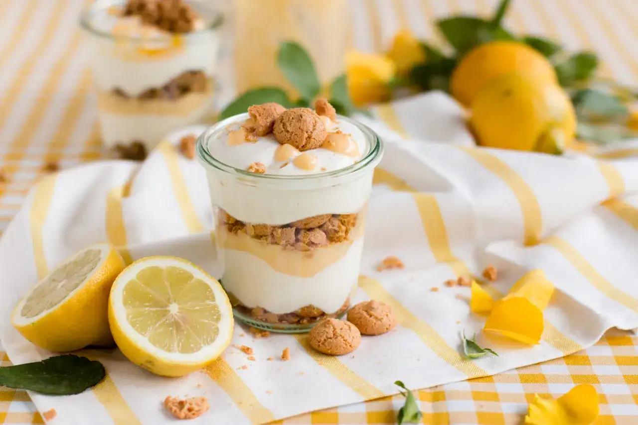 Ein Glas mit geschichtetem Limoncello Tiramisu, garniert mit Keksen und Zitronenspalten.