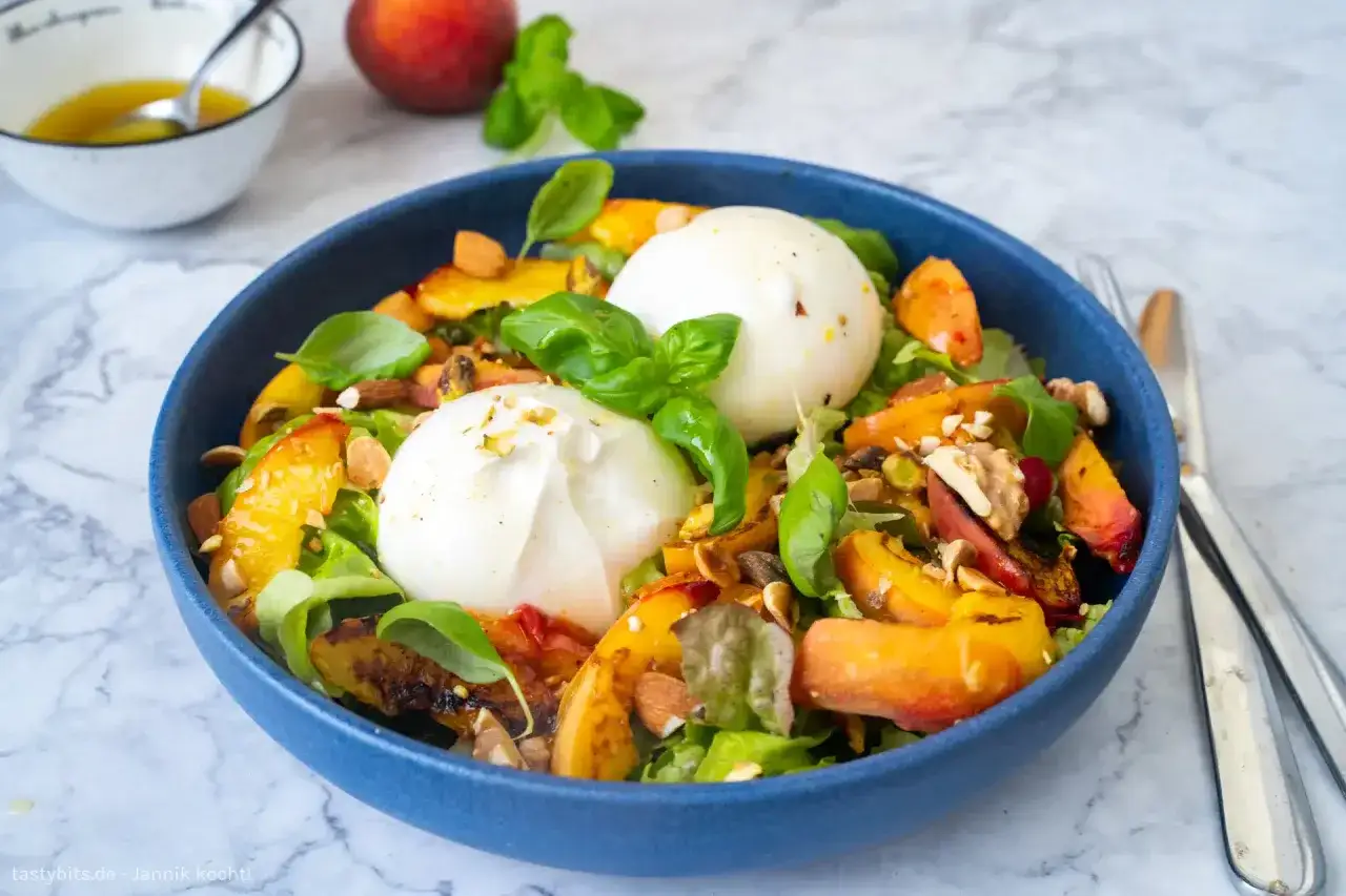 Raffinierte Sommersalate: cremiger Burrata auf gegrillten Pfirsichen, N&uuml;ssen und frischem Basilikum. Ein Genuss f&uuml;r warme Tage.