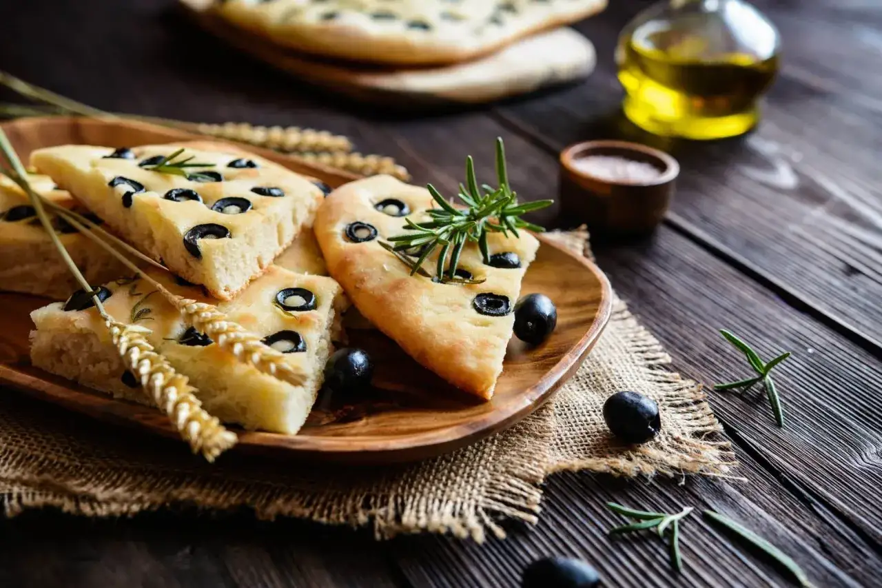 Focaccia mit Oliven, Rosmarin und Weizen&auml;hren auf einem Holzteller. Ein Hauch von Ligurien auf dem Tisch.