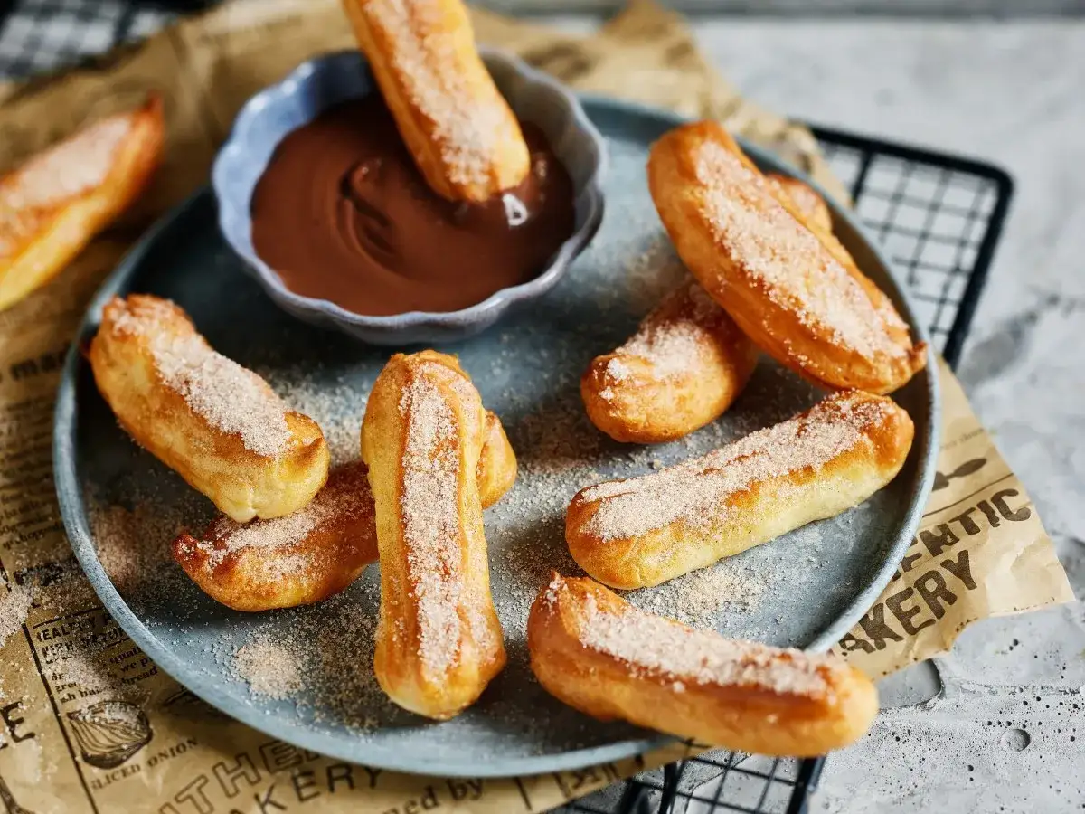 Lufterfrischte Churros, mit Zimt und Zucker bestreut, werden in eine Schüssel mit Schokoladensauce getunkt.