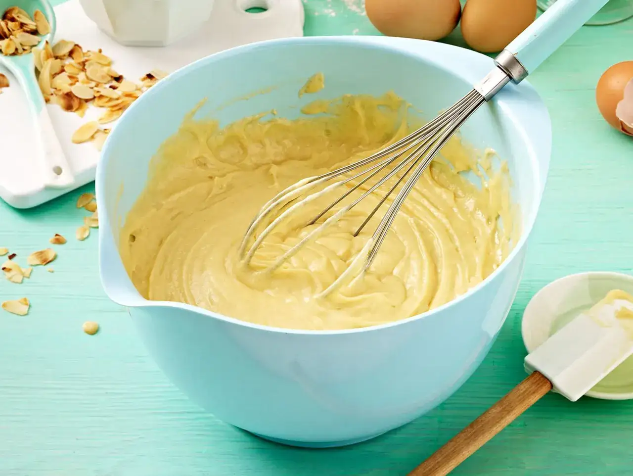 Frischer Kuchenteig wird in einer hellblauen Sch&uuml;ssel mit einem Schneebesen verr&uuml;hrt. Ein einfaches Kuchenteig Rezept f&uuml;r leckere Backwaren.