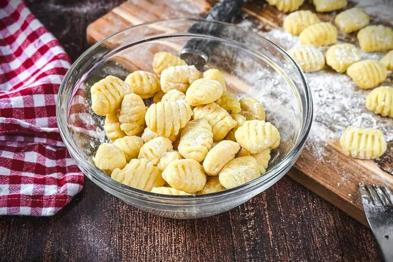 Frisch gemachte Gnocchi in einer Sch&uuml;ssel, bereit zum Kochen. Auf dem Holzbrett liegen weitere Gnocchi, die zeigen, wie einfach es ist, Gnocchi selber machen.