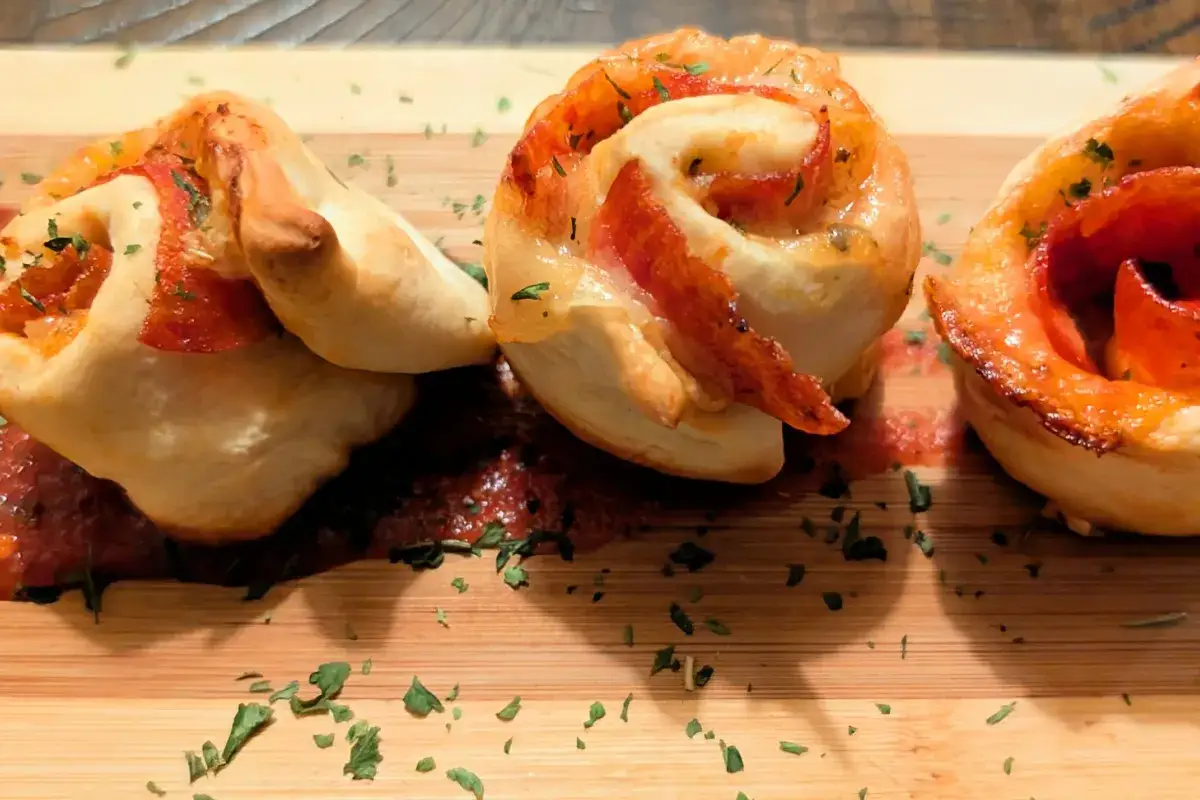 Herzhafte Pizza-Schnecken aus fertigem Teig, belegt mit Salami und K&auml;se, serviert auf einem Holzbrett mit Tomatensauce und Petersilie. Perfekt f&uuml;r schnelle herzhafte Rezepte mit fertigem Pizzateig.