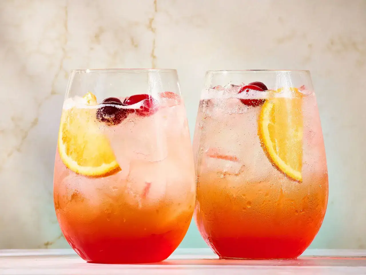 Zwei erfrischende Sarto Spritz Cocktails mit Eis, Orangenscheiben und Kirschen, bereit f&uuml;r einen sommerlichen Genuss.