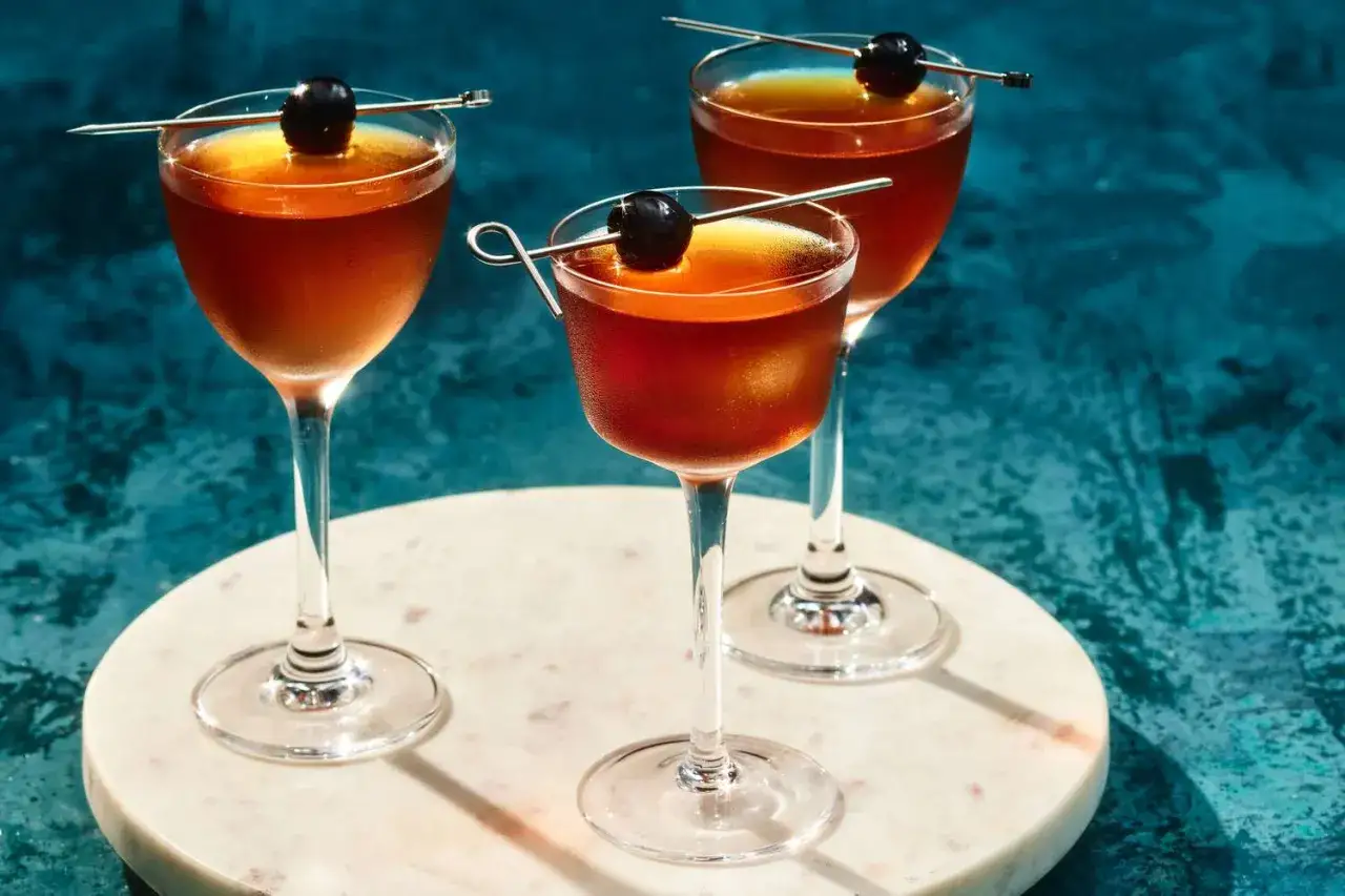 Drei elegante Gläser mit einem klassischen Cocktail aus Whisky und Wermut, garniert mit Kirschen.