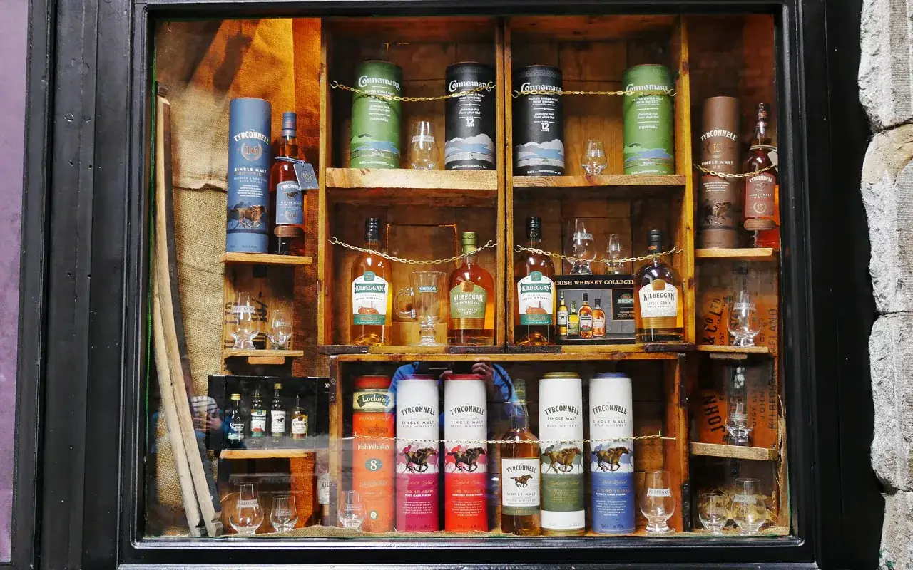 Whisky-Sortiment in einem Schaufenster, das verschiedene Flaschen und Tuben von Marken wie Tyrconnell und Kilbeggan pr&auml;sentiert. Ein ideales gin lagern f&uuml;r Kenner.