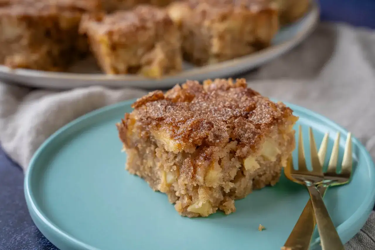 Ein Stück saftiger Apfelkuchen mit Zimtstreuseln, perfekt für ein gemütliches apfelkuchen rezept. Daneben liegen goldene Gabeln.