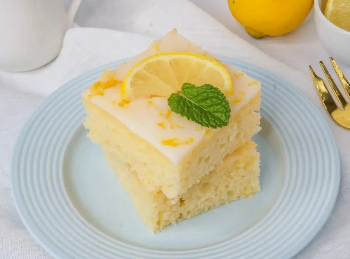 Zwei St&uuml;cke griechischer Zitronenkuchen mit Joghurt, garniert mit Zitronenscheibe und Minze, auf einem hellblauen Teller.