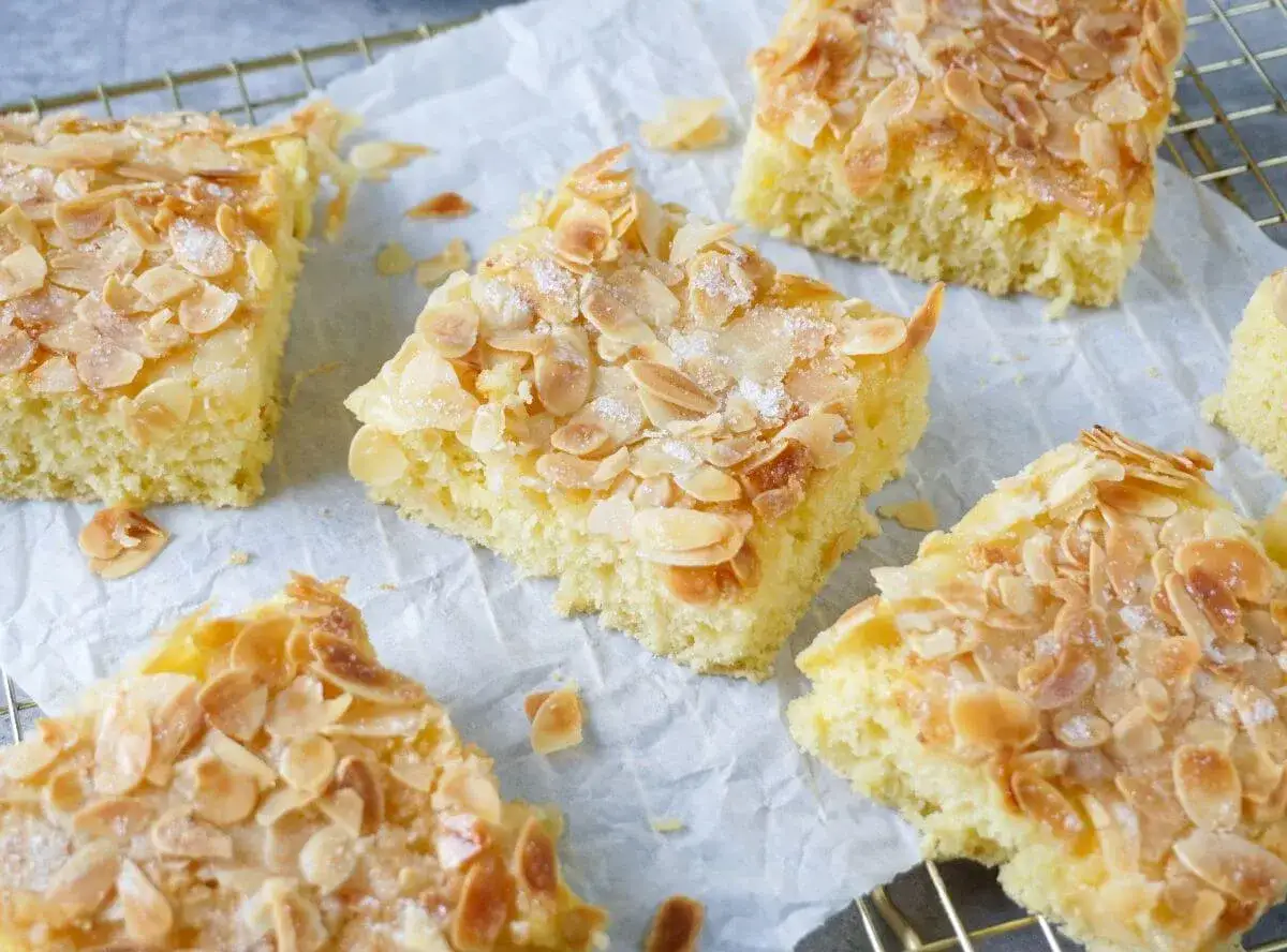 Saftiger Buttermilch Kuchen mit ger&ouml;steten Mandelbl&auml;ttchen und Zucker bestreut, auf Backpapier und einem Gitter angerichtet.