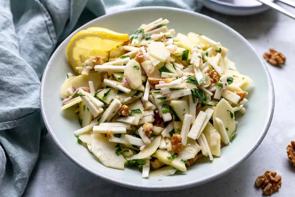 Frischer sellerie salat mit &Auml;pfeln, Waln&uuml;ssen und Kr&auml;utern, garniert mit einer Zitronenspalte.