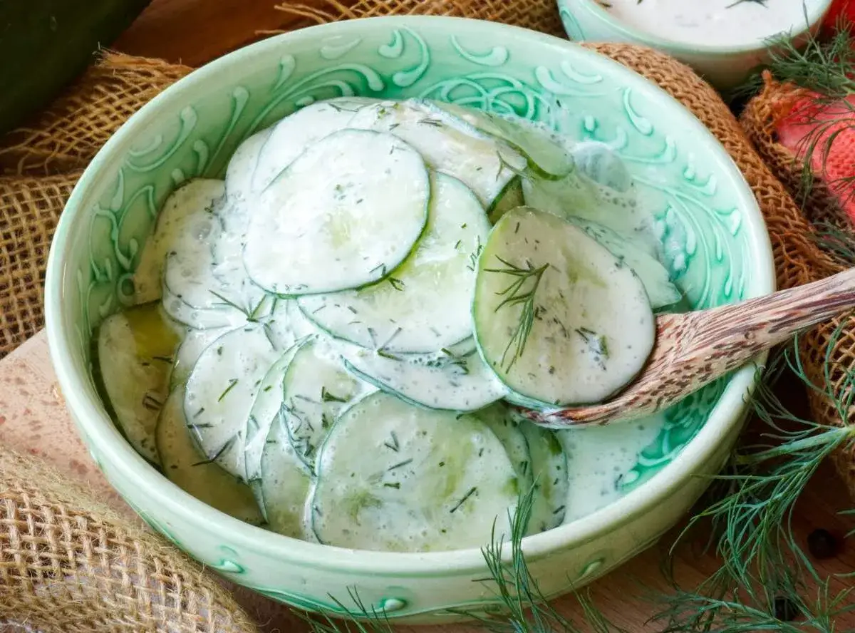 Frischer gurkensalat mit saurer sahne und dill in einer gr&uuml;nen sch&uuml;ssel, bereit zum servieren.