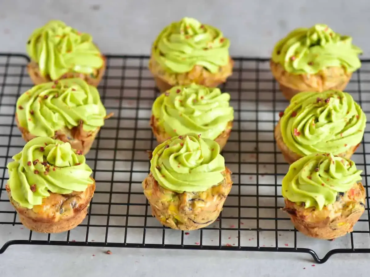 Neun herzhafte Muffins mit leuchtend gr&uuml;nem Topping, bestreut mit roten Kr&uuml;meln. Diese kleinen Leckerbissen sehen aus wie bunte regenbogen muffins.