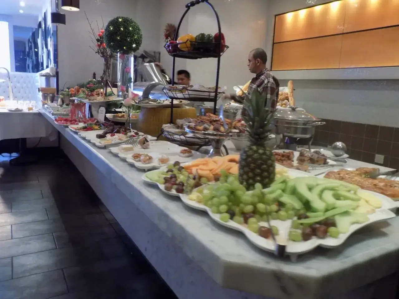 Ein Buffet mit klassischen Salaten, Obst und Geb&auml;ck. Ein Mann bedient die G&auml;ste.