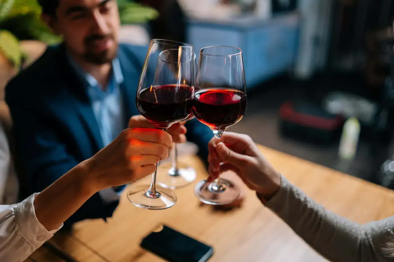 Drei Personen sto&szlig;en mit Rotwein an. Sie halten das weinglas richtig, am Stiel, um die Temperatur des Weins zu bewahren.