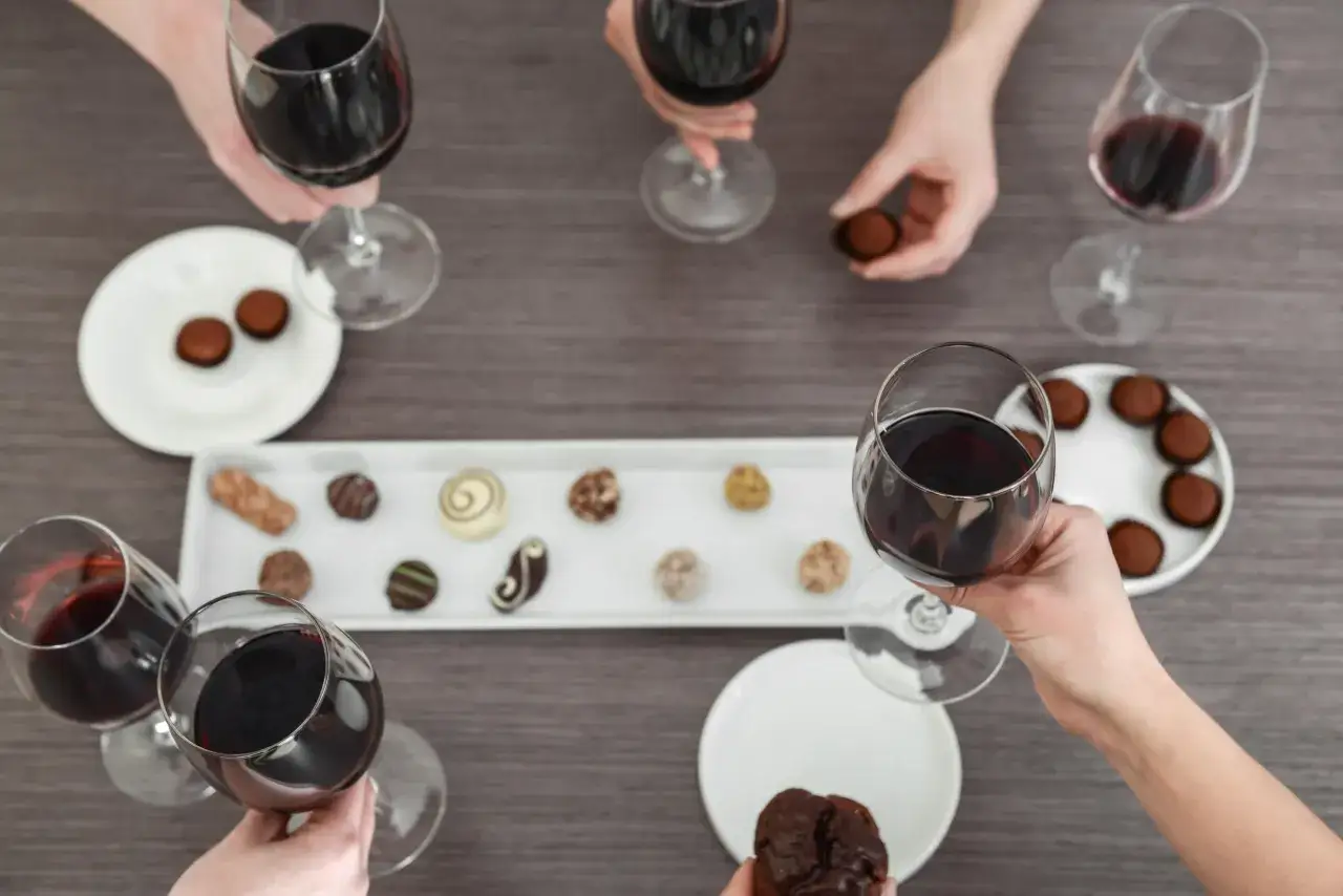 H&auml;nde reichen Gl&auml;ser mit rotwein und nehmen Pralinen. Ein Genussmoment mit rotwein mit schokolade.