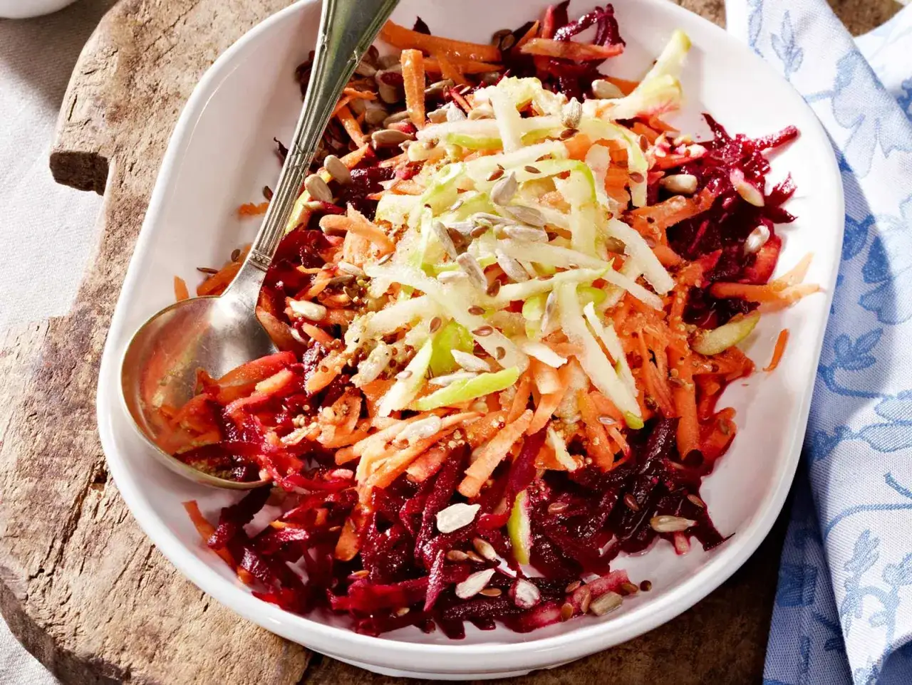 Bunter rote Bete Salat mit Apfel, Karotten und Sonnenblumenkernen, appetitlich in einer wei&szlig;en Schale serviert.