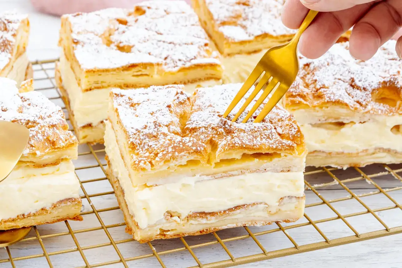 Ein goldener L&ouml;ffel sticht in ein St&uuml;ck polnischer Puddingkuchen, best&auml;ubt mit Puderzucker.