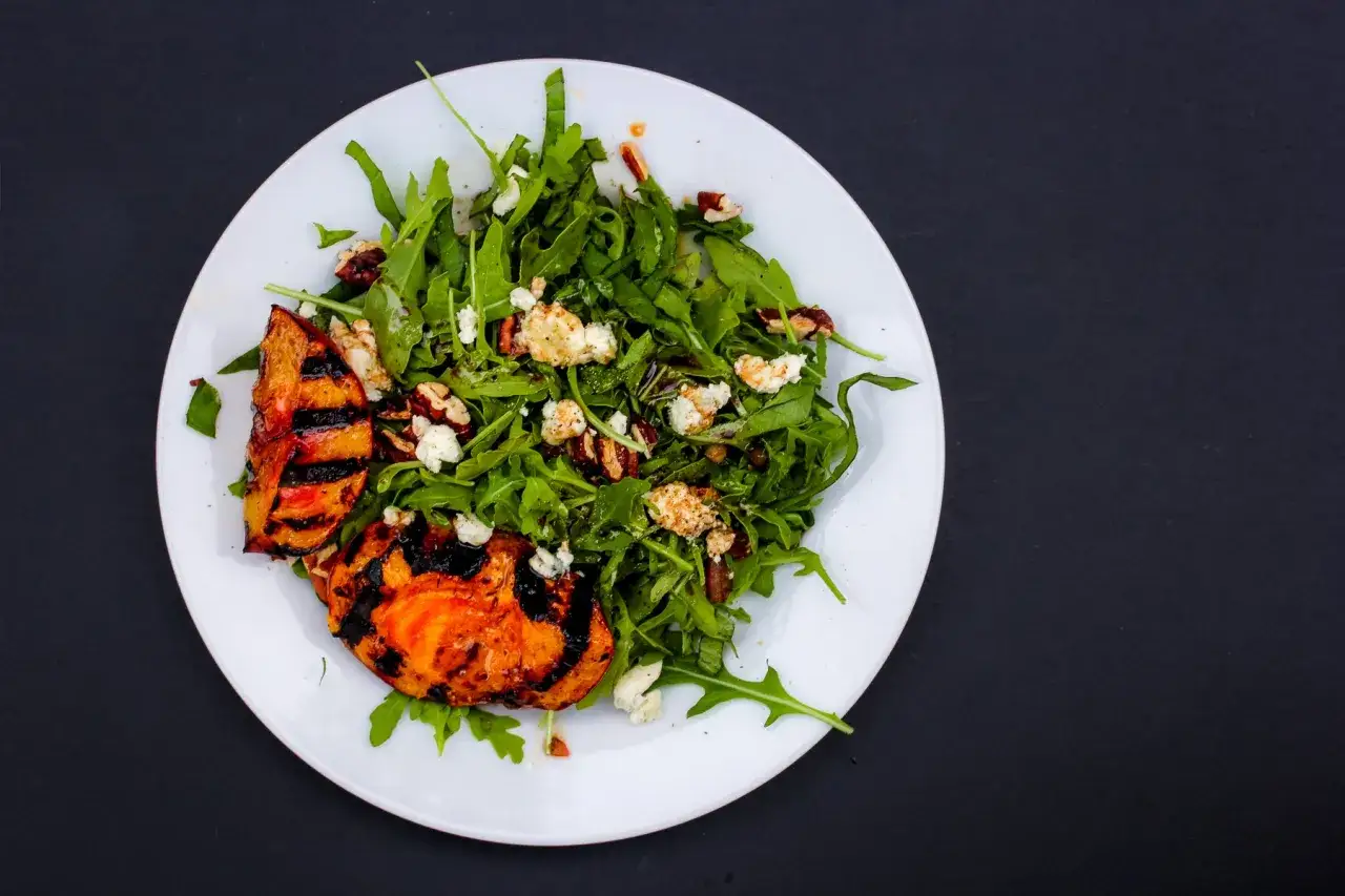 Ein frischer Salat mit Rucola, zerbr&ouml;ckeltem K&auml;se und N&uuml;ssen, garniert mit gegrillten Nektarinen.
