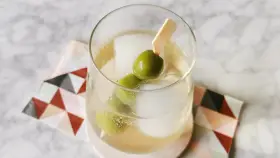 Erfrischender Italicus Spritz mit Eiswürfeln und Oliven auf einem gemusterten Untersetzer.