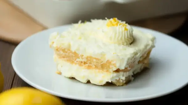Ein Stück cremiges Limoncello Tiramisu, garniert mit Zitronenzesten und einem Tupfer Sahne, auf einem weißen Teller.