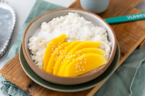 Schüssel mit cremigem **sticky rice** und saftigen Mangoscheiben, bestreut mit Sesam. Ein köstlicher Genuss!