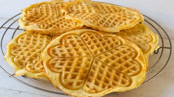 Goldbraune Herz-Waffeln, frisch gebacken aus waffelteig ohne butter, liegen auf einem Gitter.