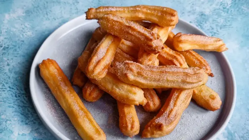 Goldbraune Churros, frisch aus dem Airfryer, mit Zucker bestreut auf einem grauen Teller.