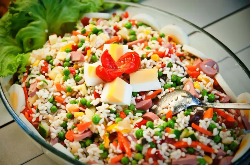 Reissalat mit Erbsen, Karotten, Ei und Wurst – ein gesunder Salat zum Grillen, garniert mit Tomaten und Salatblättern.